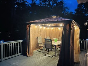 Relax in the gazebo with a table and two chairs, surrounded by a deck with a railing.