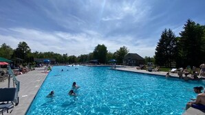 Een zwembad met mensen in het water, omringd door ligbedden en parasols.