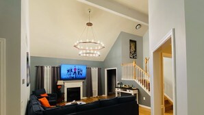 Een ruime woonkamer met een zwarte hoekbank, een televisie en een kroonluchter.