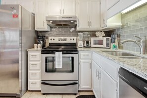 Features a kitchen with stainless steel appliances, white cabinetry, and a tiled backsplash.