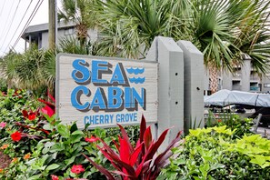Enjoy a serene beachfront stay at Sea Cabin Cherry Grove, surrounded by lush greenery and beautiful flowering plants.