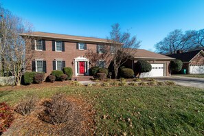 A two-story brick house with a red front door, a garage, and a well-maintained lawn.