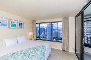 Une chambre d’hôtel avec un grand lit, une vue sur la ville et trois tableaux encadrés accrochés au mur.