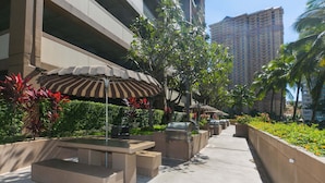 A rooftop patio with outdoor furniture, a grill, and a striped awning. - Discovery Bay, near Ala Moana Shopping Center & the Beach! (Honolulu)