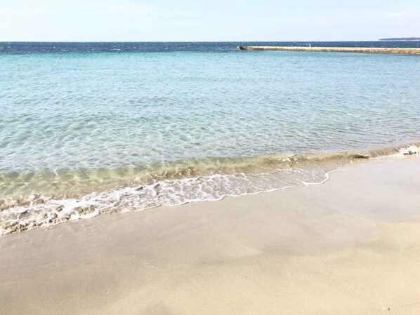 A beach with clear shallow waters and a sandy shore.