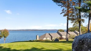 A lakeside property with a grassy lawn, a large rock, and a row of houses with sloped roofs.