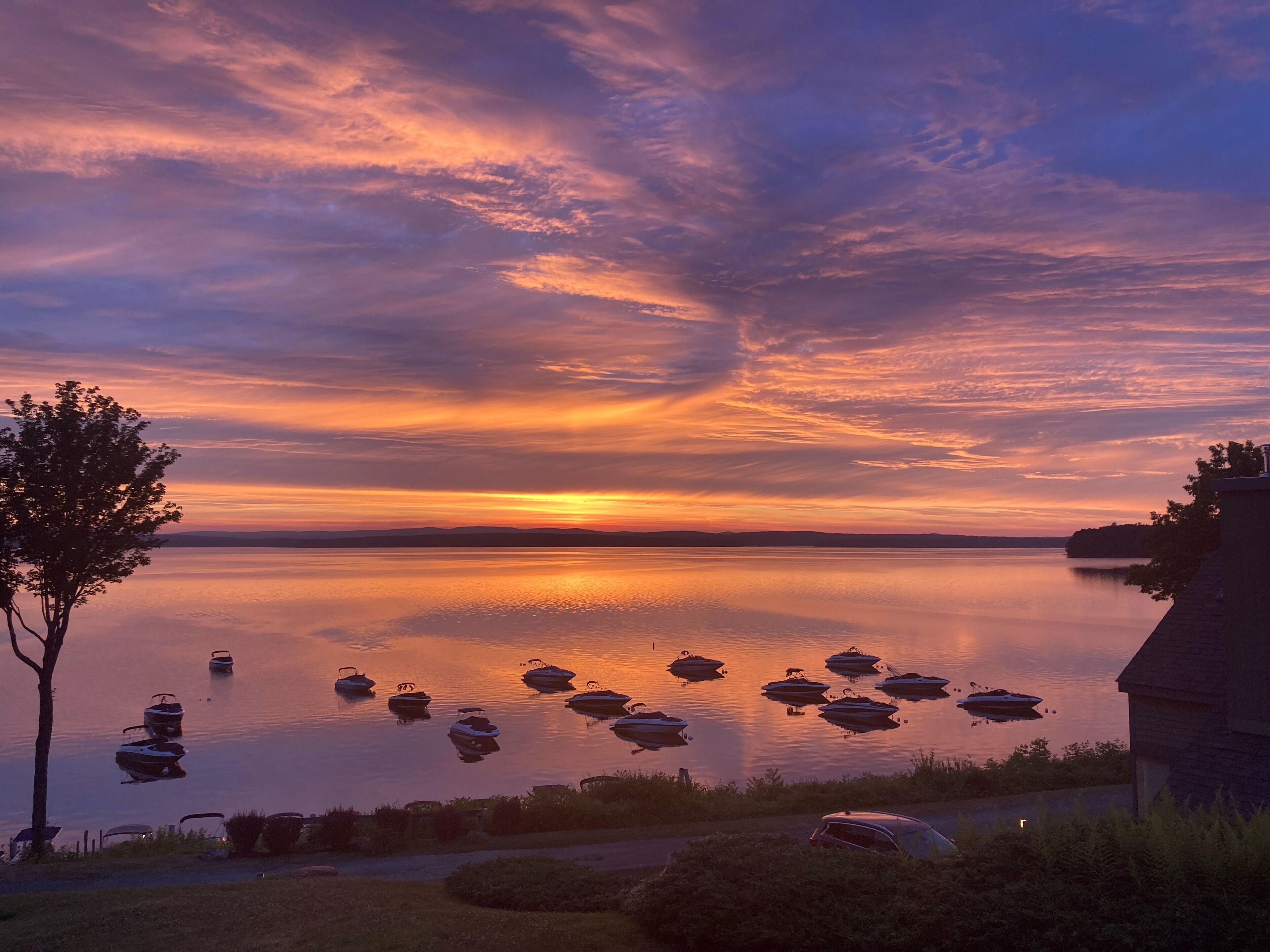 A sunset over a calm lake with several boats anchored.