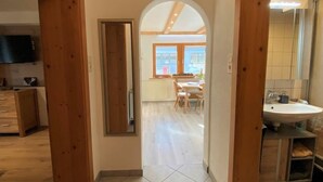 Passadís que condueix a una zona de menjador amb vista a l'exterior, cuina amb armaris de fusta i bany amb rentamiques i mirall.