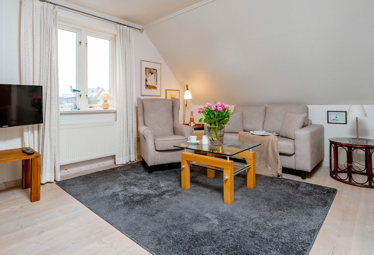 Ein modernes Wohnzimmer mit Fernseher, zwei Sofas, einem Glastisch und Blick auf die Stadt durch ein großes Fenster.