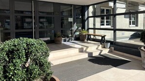 Moderni rakennus, jossa on suuret lasi-ikkunat, yläkertaan johtavat portaat ja pieni penkki ulkona.