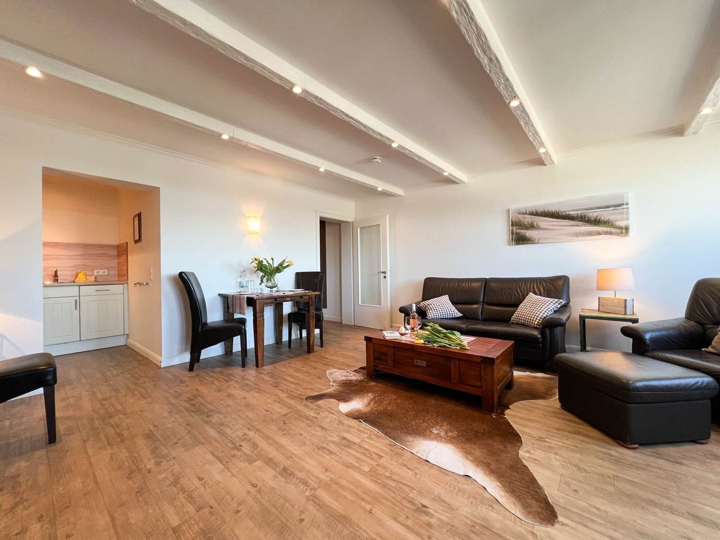 A modern living room with a wooden floor, a leather sofa, a coffee table, and a dining area with a table and chairs.