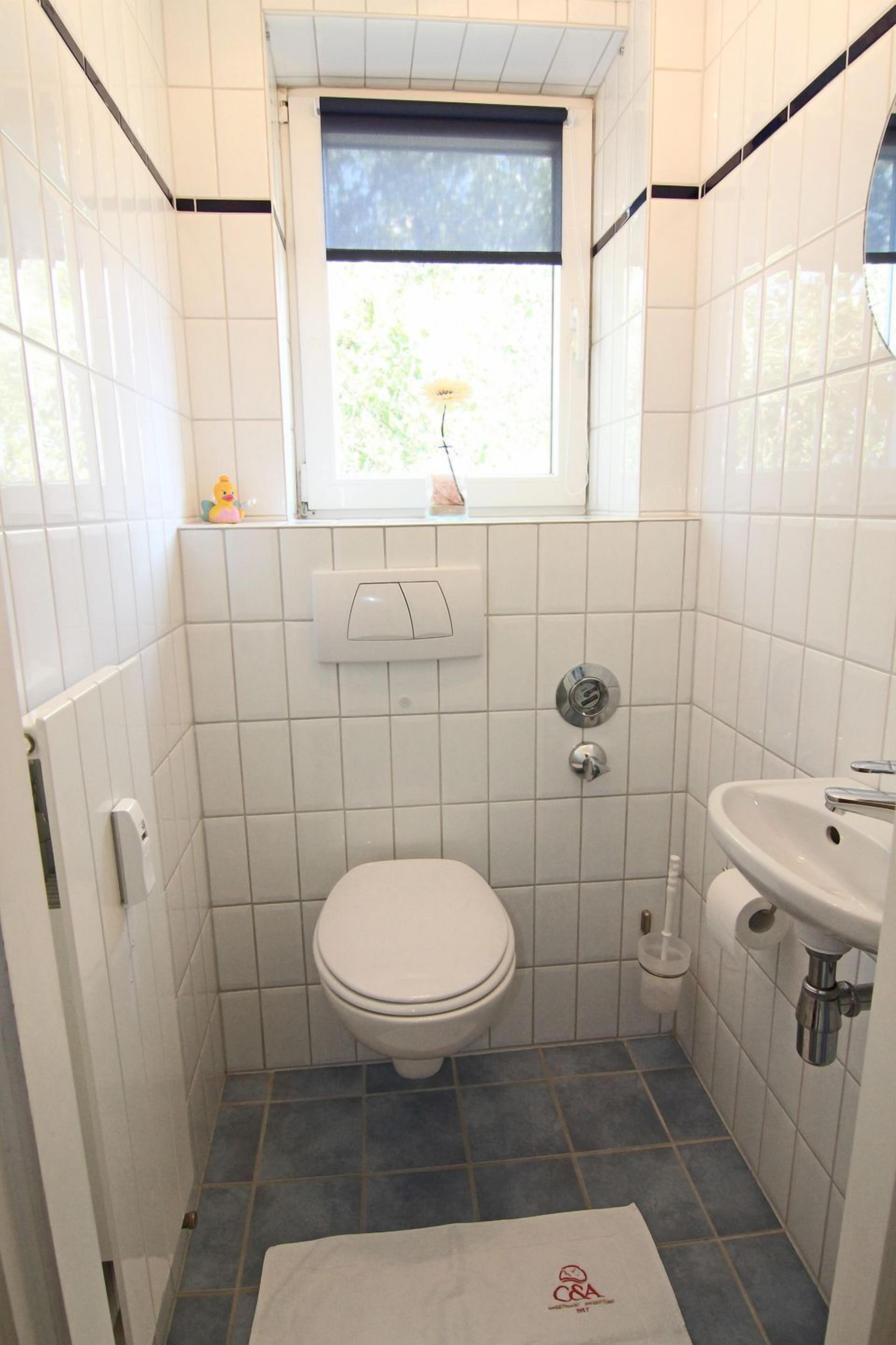 A small, tiled bathroom with a toilet, sink, and window.