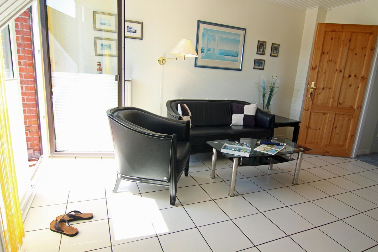 A modern living room with a black leather sofa, a glass coffee table, and a tiled floor.