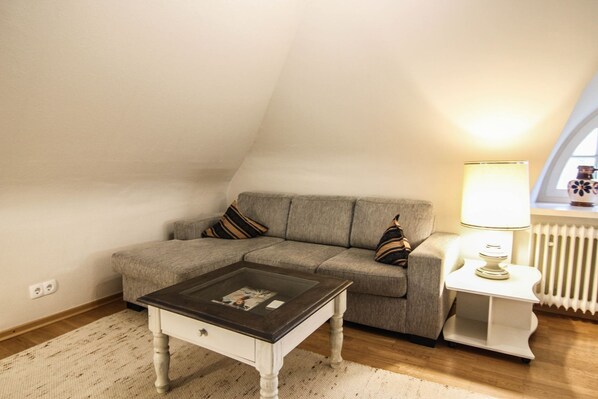 A cozy loft bedroom with a gray sofa, a small white side table with a lamp, and a wooden coffee table.