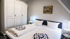 A bedroom with a large bed, a wardrobe, a bedside table with a lamp, and a painting on the wall.