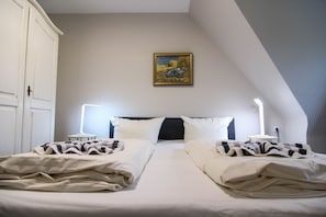 A bedroom with a large bed, two bedside tables, a nightstand, a painting, and a sloped ceiling.