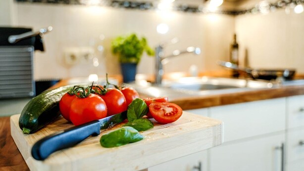 Una encimera de cocina con verduras frescas, un cuchillo y una planta al fondo.