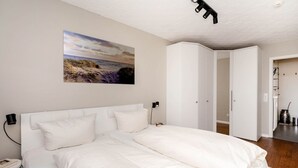 Un dormitorio con una cama grande, una mesita de noche, una lámpara de pared y un cuadro de una playa.