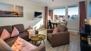 Una sala de estar moderna con un conjunto de sofá, una mesa de centro con frutas, un televisor y una zona de comedor con una mesa y sillas.
