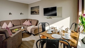 Una sala de estar moderna con un sofá, una mesa de centro, una mesa de comedor y sillas. Hay un televisor de pantalla plana montado en la pared y un cuadro encima.