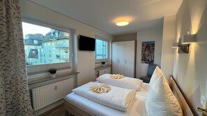 A bedroom with a bed, a window, a TV, and a radiator. - By the sea - A modern and bright vacation apartment in the heart of Westerland. (Sylt)
