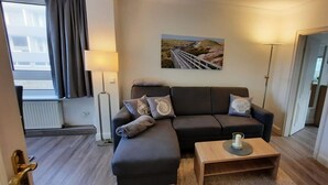 A modern living room with a sofa, a coffee table, and a painting on the wall. - By the sea - A modern and bright vacation apartment in the heart of Westerland. (Sylt)
