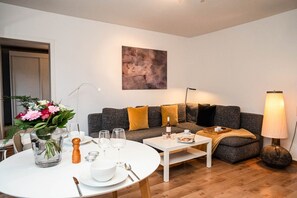 Una sala moderna con un sofá gris, una mesa de centro blanca y una mesa de comedor preparada para dos comensales.