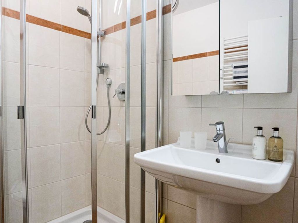 A bathroom with a glass-enclosed shower, a sink with toiletries, and a mirror with a towel rack.