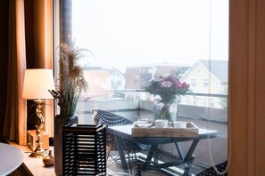 Un balcón con una mesa, sillas, un florero con flores, una lámpara y vistas a edificios.