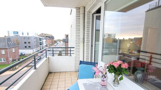 A balcony with a table, a chair, a vase with flowers, and a bottle of champagne. - Austernfischerin - A modern and bright vacation apartment in the heart of (Sylt)
