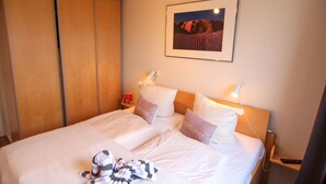 A hotel room with a large bed, a wardrobe, a bedside table with a lamp, and a framed picture on the wall. - Austernfischerin - A modern and bright vacation apartment in the heart of (Sylt)