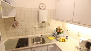 A kitchen with a sink, stove, and countertop. There is a clock on the wall, a dish rack, and a vase with flowers. - Austernfischerin - A modern and bright vacation apartment in the heart of (Sylt)