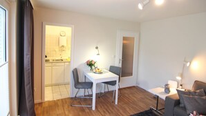 A compact living space with a dining area, kitchenette, and a seating area with a sofa and a small table. - Austernfischerin - A modern and bright vacation apartment in the heart of (Sylt)
