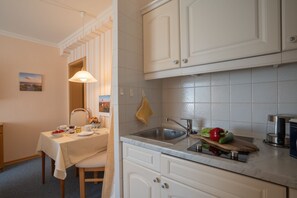 Et køkken med hvide skabe, en vask og et spiseområde med et bord dækket til to.