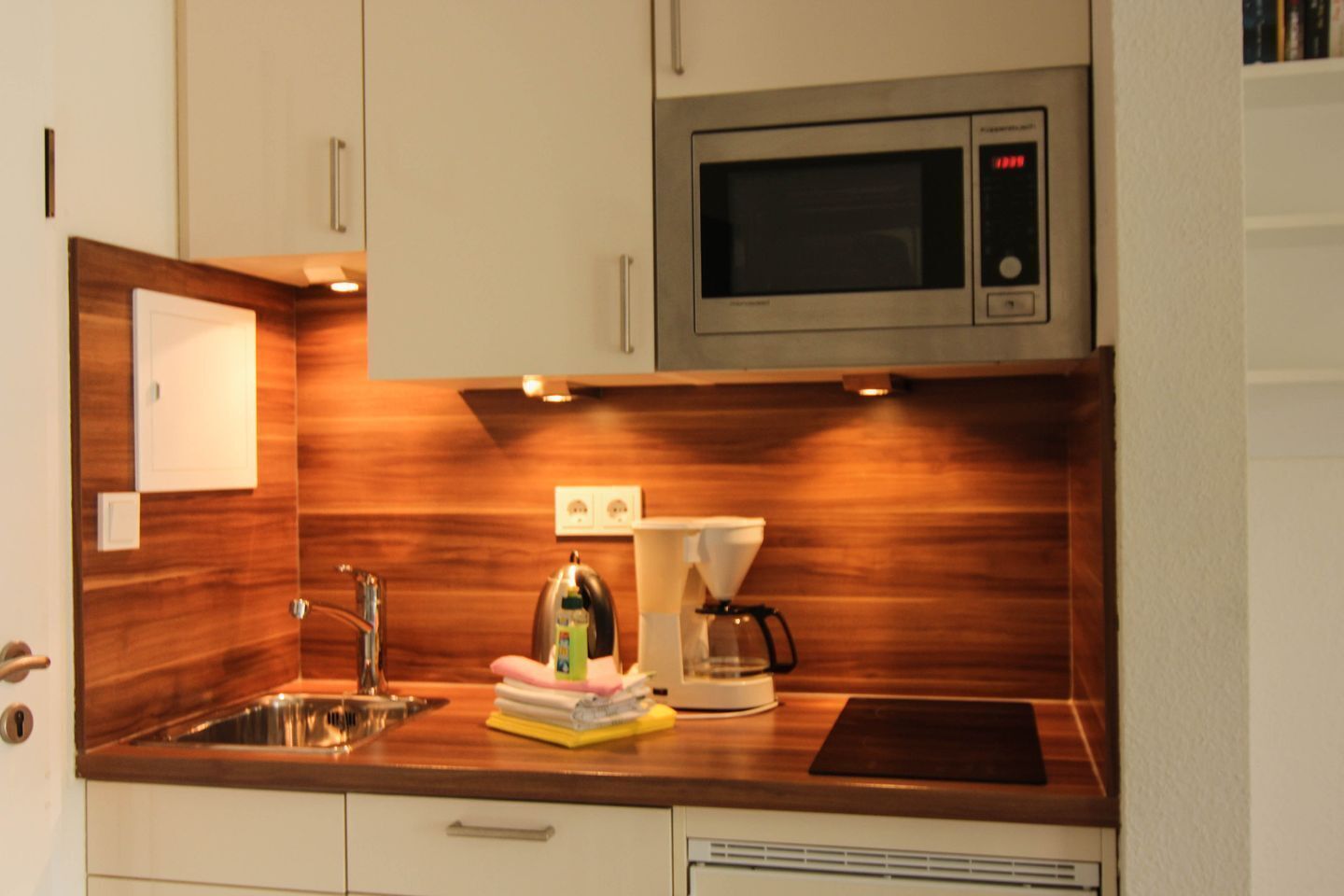 Una cocina compacta con microondas integrado, cafetera y lavamanos.