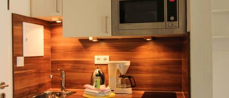 Una cocina compacta con microondas integrado, cafetera y lavamanos.