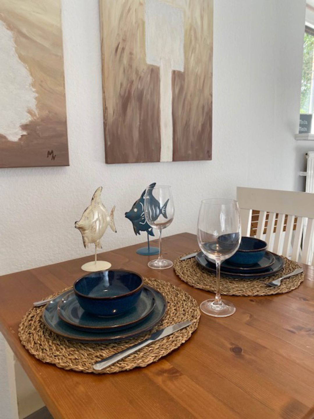 A wooden dining table with blue plates, clear wine glasses, and a decorative fish sculpture.