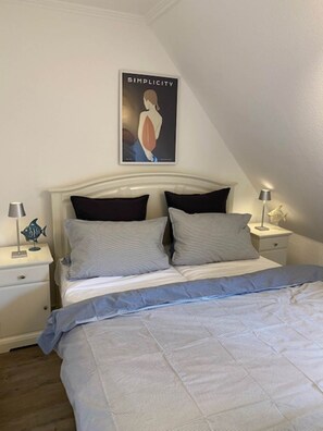 A bedroom with a bed, two nightstands, a poster on the wall, and a lamp on one nightstand. - Anja - A modern and bright vacation apartment in the heart of Westerland. (Sylt)