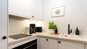 Une cuisine moderne avec des meubles blancs, un four encastré, une machine à café, un évier et une plante en pot.