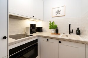 A modern kitchen with white cabinetry, a built-in oven, a coffee maker, a sink, and a potted plant.
