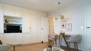 Un salon moderne doté d’un téléviseur à écran plat, d’une table à manger avec des chaises, d’une table basse agrémentée d’objets décoratifs et d’une grande armoire blanche avec des étagères.