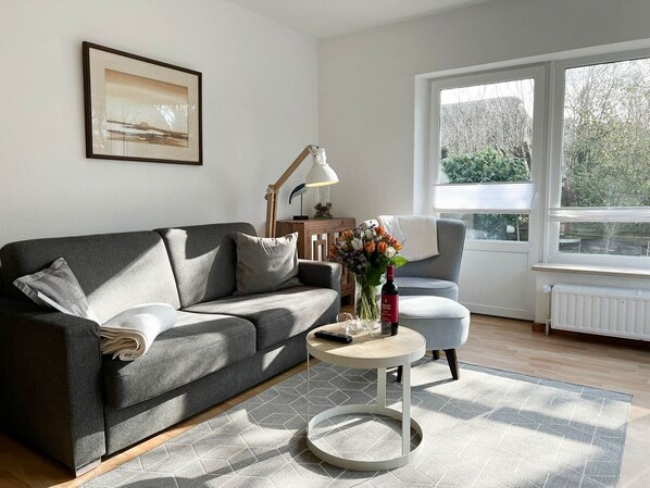 Un salon moderne avec un canapé gris, une table basse ronde et une table d’appoint sur laquelle se trouvent une lampe et des fleurs.