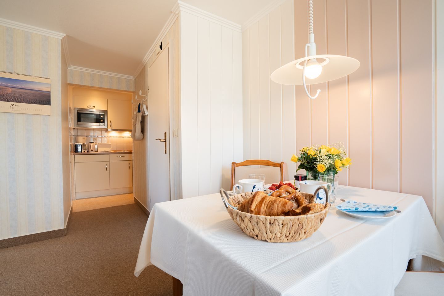Ein Zimmer mit Esstisch, gedecktem für das Frühstück, einer Mikrowelle in der Küche und einer Hängelampe.