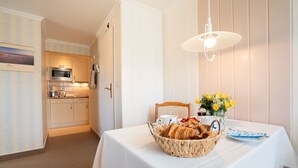 Una habitación con una mesa de comedor dispuesta para el desayuno, un microondas en la cocina y una lámpara colgante.
