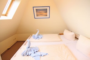A small, triangular room with two beds, a framed picture on the wall, and a skylight.