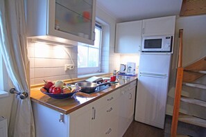 A compact kitchen with white cabinets, a microwave, a coffee maker, and a bowl of fruit on the counter.