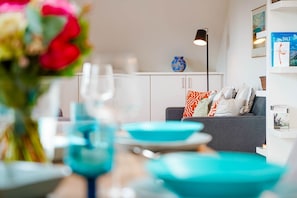 A modern living room with a grey sofa, teal bowls, and a vase with red flowers.