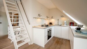 Une cuisine moderne avec des meubles blancs, un four encastré et un escalier en bois.