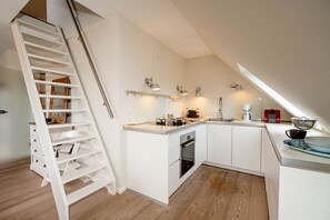 A modern kitchen with white cabinetry, a built-in oven, and a wooden staircase.