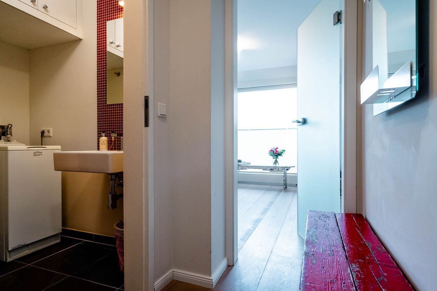A hallway with a white door leading to a balcony with a view.